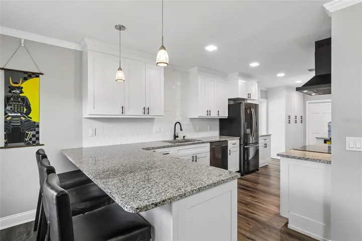 Kitchen Breakfast Bar – The kitchen features a spacious granite breakfast bar with pendant lighting and seating space, creating an inviting spot for casual dining. White cabinetry, a tile backsplash, and dark hardware add a clean, updated look.