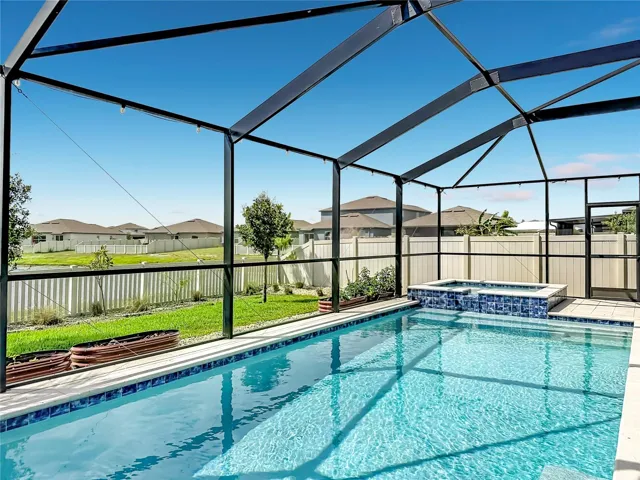 Backyard oasis featuring an enclosed heated saltwater pool and spa, expansive paver decking, and tranquil pond views