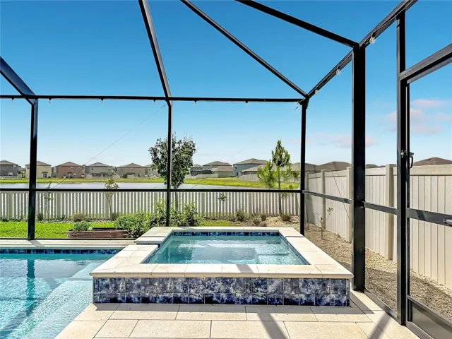 Backyard oasis featuring an enclosed heated saltwater pool and spa, expansive paver decking, and tranquil pond views