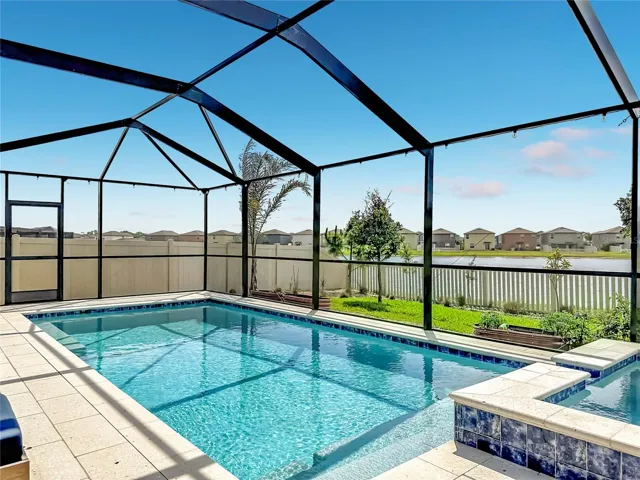 Backyard oasis featuring an enclosed heated saltwater pool and spa, expansive paver decking, and tranquil pond views