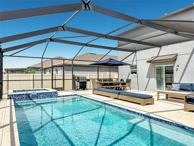 Backyard oasis featuring an enclosed heated saltwater pool and spa, expansive decking, and tranquil pond views