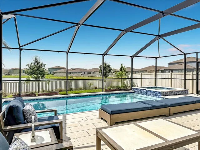 Backyard oasis featuring an enclosed heated saltwater pool and spa, expansive paver decking, and tranquil pond views