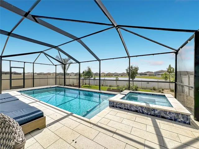 Backyard oasis featuring an enclosed heated saltwater pool and spa, expansive decking, and tranquil pond views