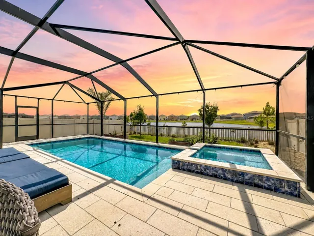 Backyard oasis featuring an enclosed heated saltwater pool and spa, expansive decking, and tranquil pond views