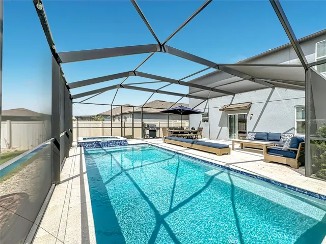 Backyard oasis featuring an enclosed heated saltwater pool and spa, expansive paver decking, and tranquil pond views