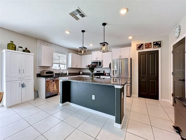 Well-appointed kitchen with granite countertops, spacious island with breakfast bar seating, stainless steel appliances, subway tile backsplash, abundant cabinetry, and updated pendant lighting