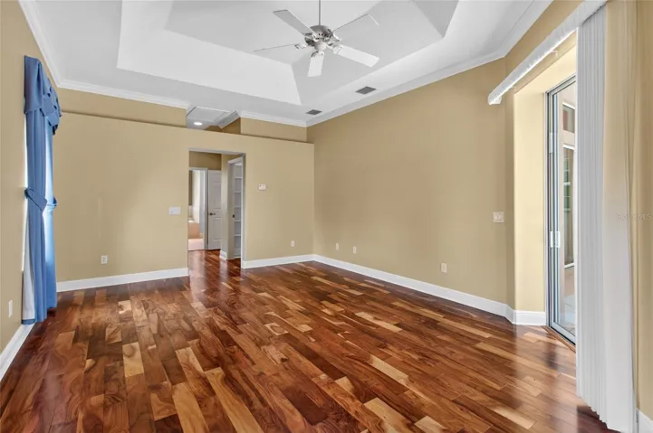 PRIMARY BEDROOM WITH HARDWOOD FLOORING, TRAY CEILING, AND SLIDING GLASS DOORS THAT OPEN TO THE LANAI.