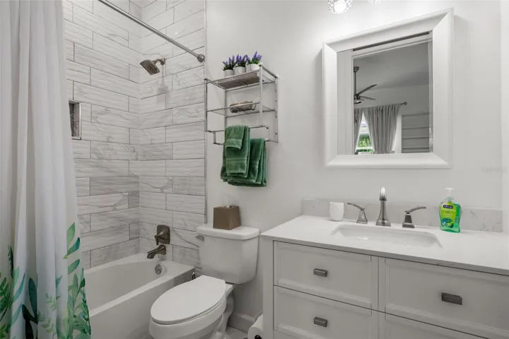 Bedroom 3 ensuite bath features a tub with shower, marble-look tile extending to the ceiling, a mirrored vanity with quartz countertop, upgraded fixtures, and a built-in shower niche.