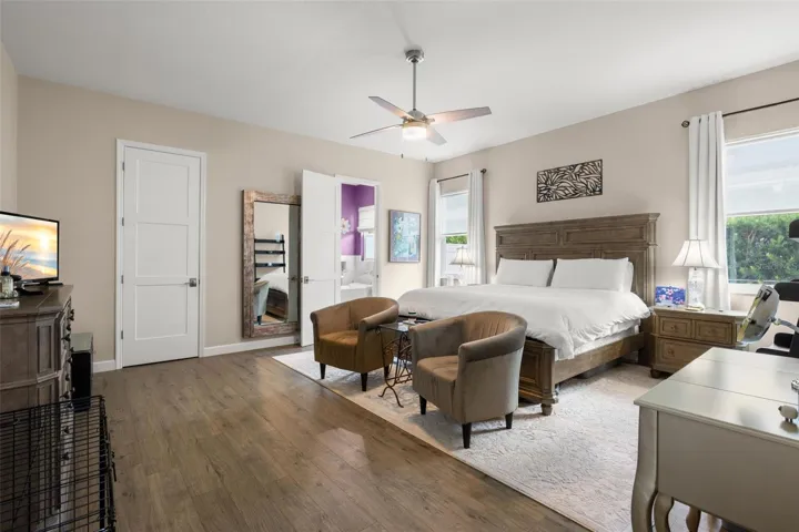 The oversized primary bedroom features wide-plank luxury vinyl flooring, neutral finishes, oversized paneled doors, and a contemporary ceiling fan. With room for a sitting area and direct access to the ensuite bath and walk-in closet, the spacious layout offers both comfort and functionality.