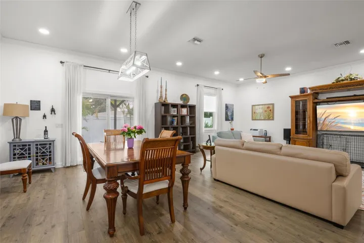 Oversized impact sliding glass doors and large windows fill the dining and living areas with natural light, complementing the home’s high ceilings, crown molding, recessed lighting, and wide-plank luxury vinyl flooring. The open layout offers generous wall space and flexible furniture placement throughout the main gathering areas.