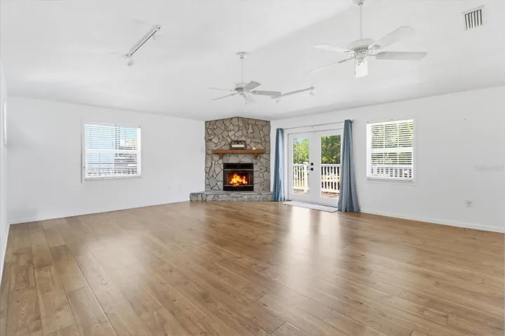 Living Room w/ PERGO Laminate Flooring, French Doors to the Upper Level Wrap Around Wood Deck & PreFab Wood Burning Fireplace w/ Stone Veneer Surround, Cedar Mantle & Prewiring for Blower