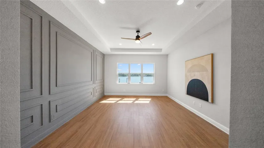 Spacious primary suite with tray ceiling, custom wall detailing, and lake views