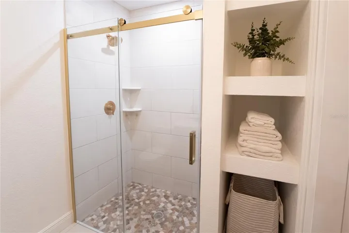 Tile walk-in shower and glass shower door with storage in primary bathroom