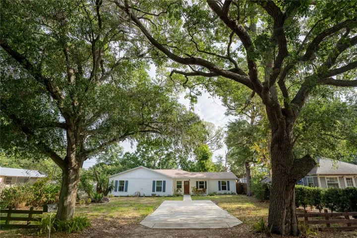 Front of home with large yard and trees at the end of driveway