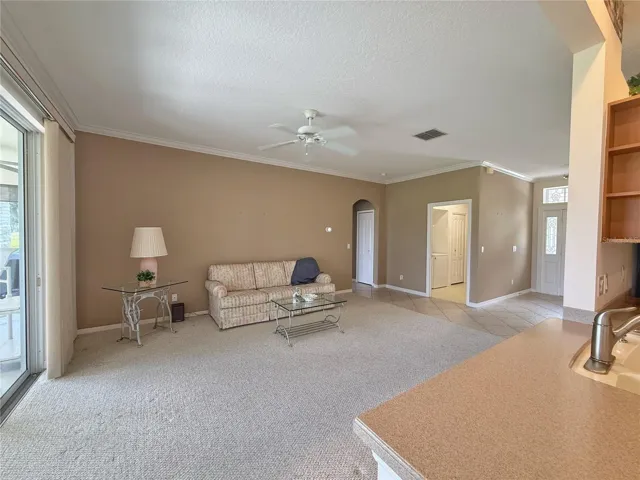 Living room from Kitchen with crown molding, view of laundry room and front door, stackable sliding glass doors leading onto covered and screened in lanai