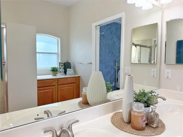 Primary Bathroom with dual sinks, solid wood cabinets, ceramic tile flooring, Corian countertops, shower , water closet, walk in closet