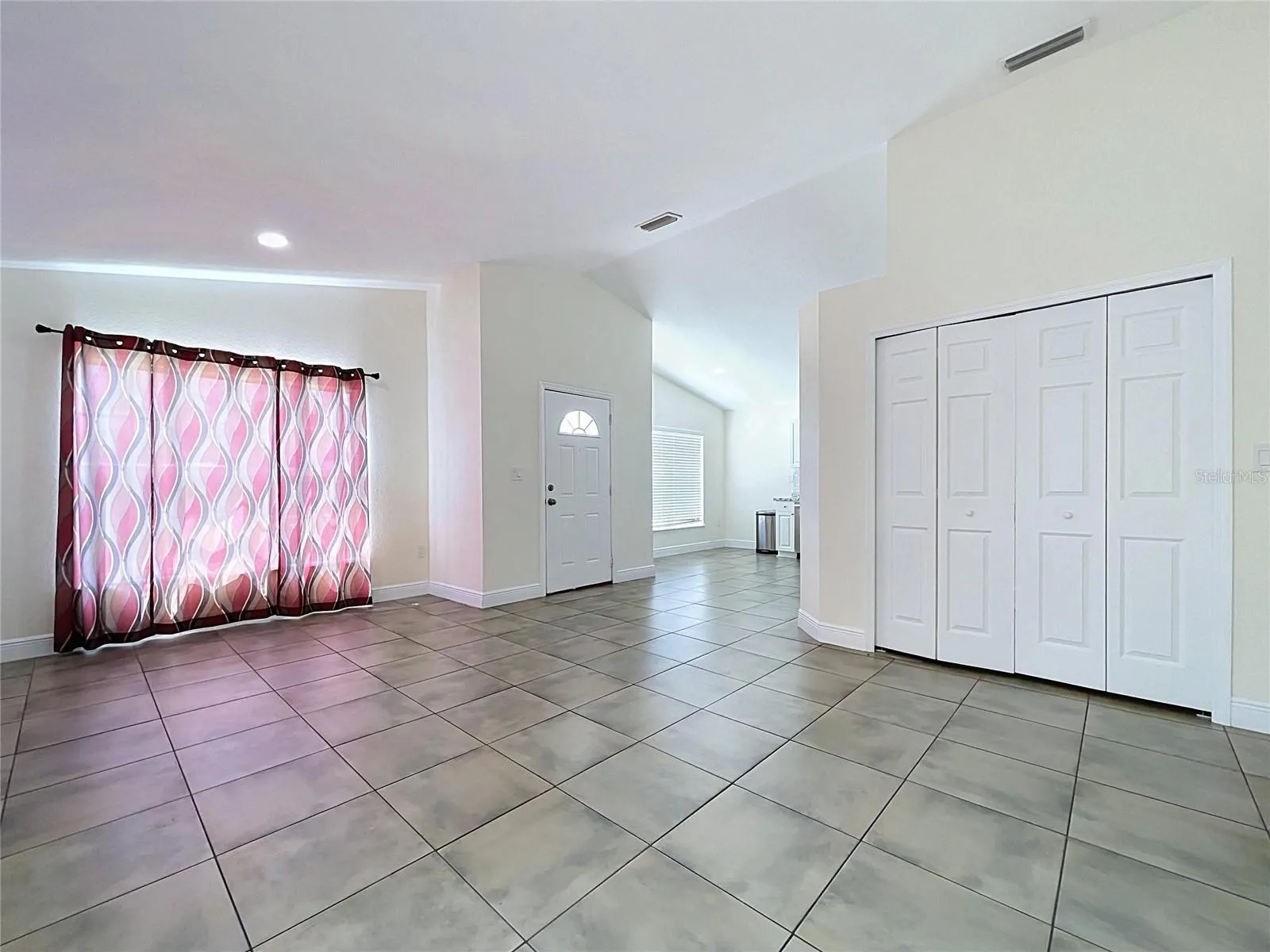 Main House Interior View Entering Front Door Highlighting Ceramic Floor in Living Room on Right Side Showing Curtained Front Oversized Windows and Kitchen and Dinette on Left Side On Left Side
