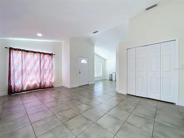 Main House Interior View Entering Front Door Highlighting Ceramic Floor in Living Room on Right Side Showing Curtained Front Oversized Windows and Kitchen and Dinette on Left Side On Left Side
