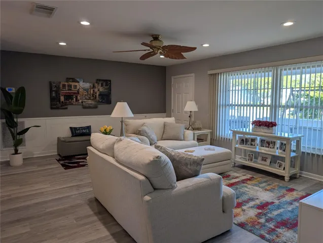 View of living room to front entry from hallway. Completely renovated in 2005 to studs, interior renovated again in 2023...neutral gray decor, wainscoting, beautiful luxury vinyl flooring, removal of popcorn ceilings, new ceiling fans, recessed lighting.