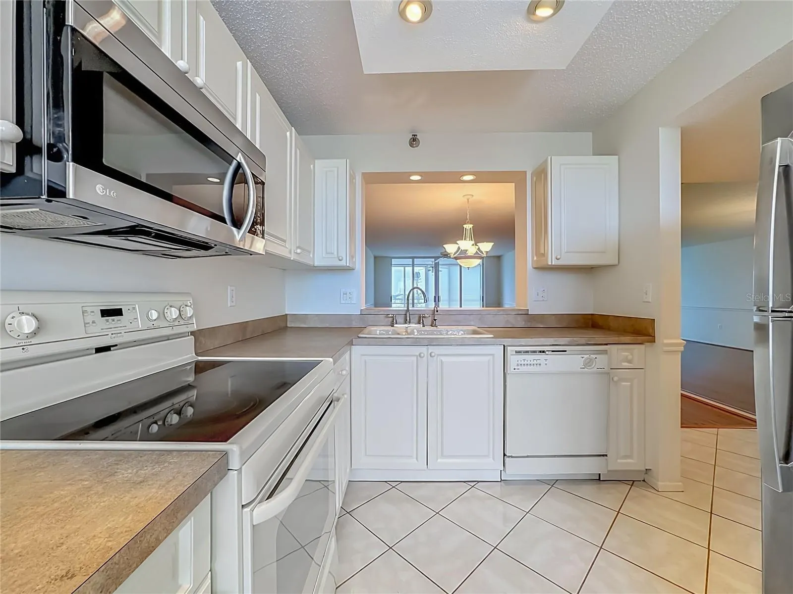 Kitchen with white cabinets and stainless steel microwave and refrigerator.  Pass through to the dining room.