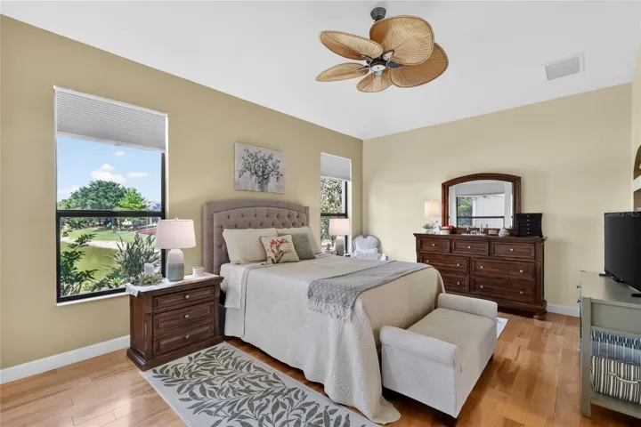 Primary bedroom with wood flooring, tropical ceiling fan, and views of the water