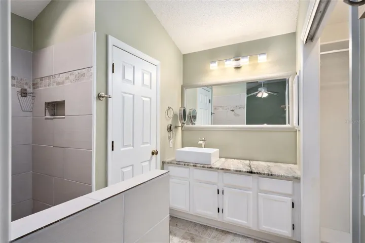 ENSUITE PRIMARY BATHROOM - Renovated shower to tiled ROMAN SHOWER (L), private water closet (closed door on L), single vessel sink with waterfall faucet, updated lighting fixture (top center), and GRANITE COUNTERTOPS.