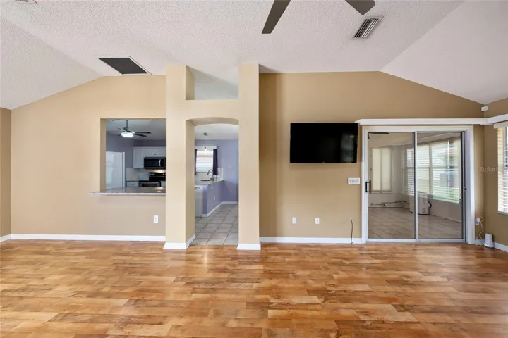 View of main living area shows DECORATIVE ARCHWAY w/ plant shelf leading to the KITCHEN. Note PASS THROUGH WINDOW on L and SLIDING GLASS DOORS on R leading to the ENCLOSED LANAI.