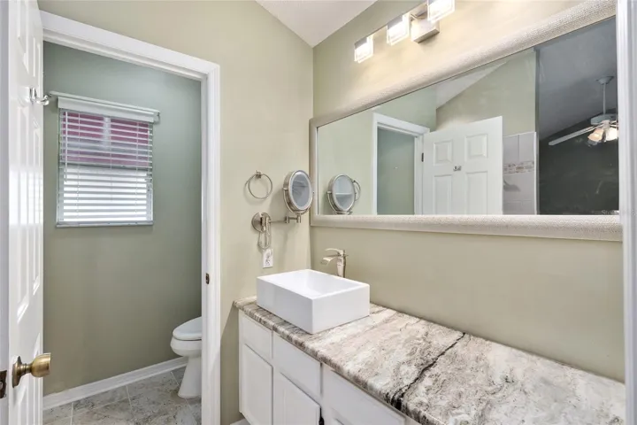 ENSUITE PRIMARY BATHROOM - Private Water Closet w/ COMFORT HEIGHT TOILET (back L), framed mirror, updated lighting fixture, and single sink/vanity with GRANITE COUNTERTOP