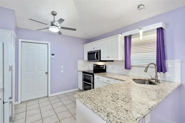 KITCHEN features WHITE cabinets w/ crown molding, subway TILE BACKSPLASH, GRANITE COUNTERTOPS, newer SS APPLIANCES - Electric double RANGE (2022), MICROWAVE (2022), FISHER & PAYKEL DISHWASHER (2019) and REFRIGERATOR. Note upgraded ceiling fan and pendant lighting over the undermount sink w/ pull down faucet.