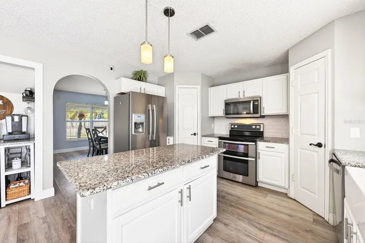 The beautifully updated kitchen is designed for both everyday living and entertaining, showcasing a fresh neutral color palette, granite countertops, subway tile backsplash, FARMHOUSE SINK, prep ISLAND, STAINLESS STEEL APPLIANCES, DUAL PANTRIES for exceptional storage, and a window over the sink.