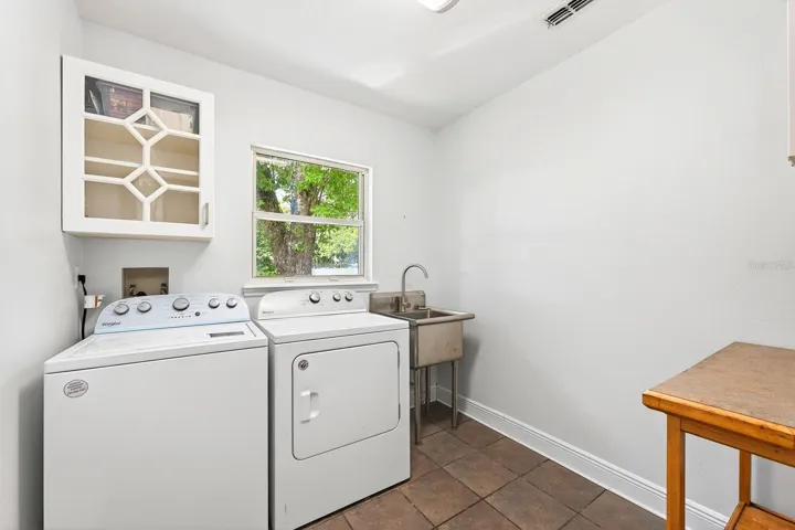 The spacious Laundry Room is thoughtfully equipped with a STAINLESS STEEL UTILITY TUB, cabinetry, folding table, and included washer and dryer.