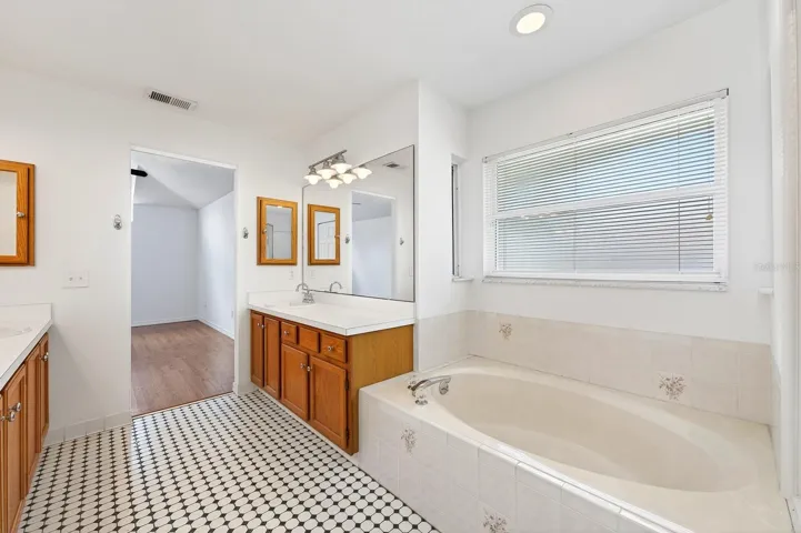 An ELEGANT EN SUITE BATH in the Primary Suite features dual vanities, beautiful tile flooring, a garden tub, and separate step-in shower.