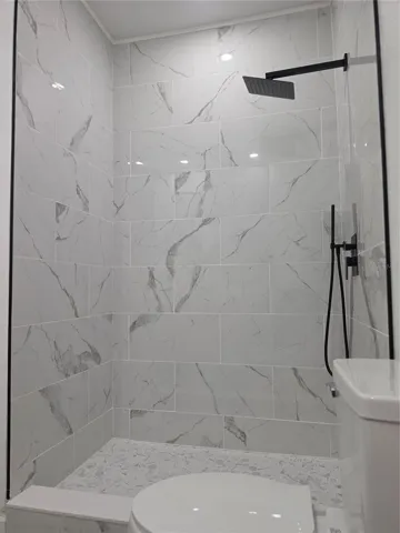 Stylish modern bathroom with a sleek tiled walk-in shower, contemporary matte black fixtures, and upscale marble-look tile throughout.
