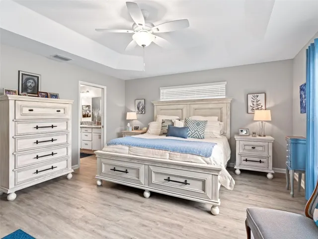 The serene primary bedroom offers natural light, architectural tray ceilings, beautiful vinyl flooring, and a well-appointed en suite bath.