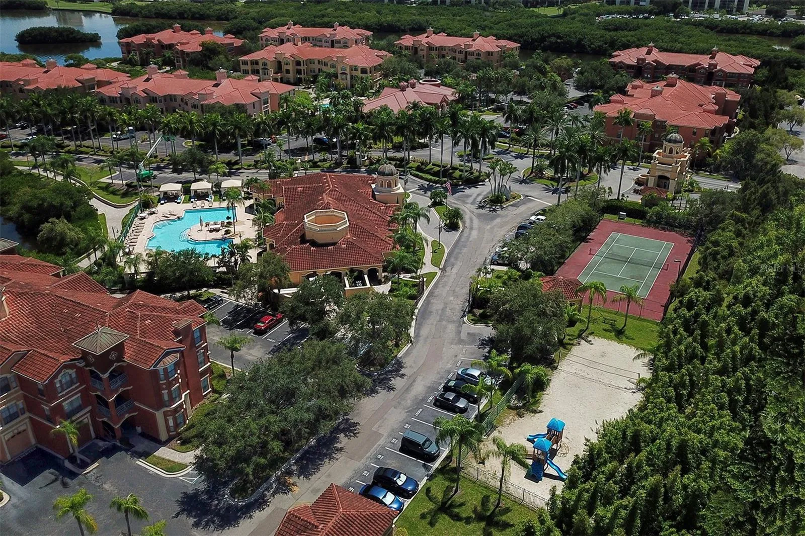 Aerial photo of the clubhouse and pool to the left, playground and sand volleyball court to the right and tennis court and guardhouse toward the top right