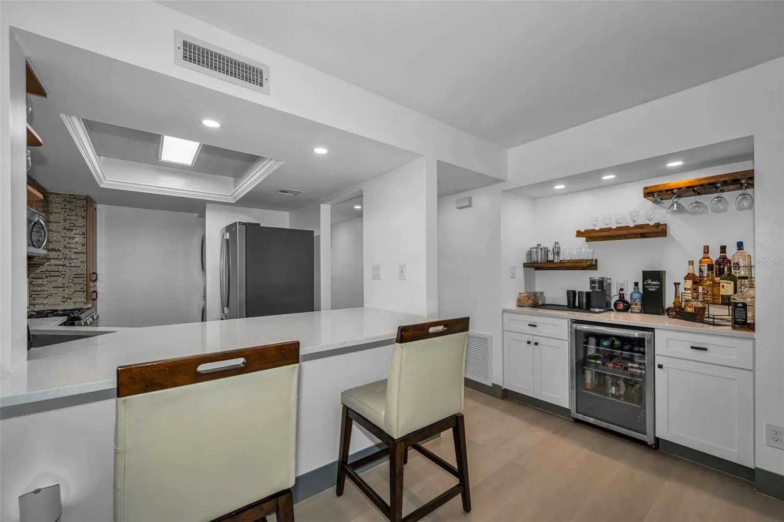 Another view of dry bar with wine refrigerator and storage cabinets, plus stools at open kitchen bar.