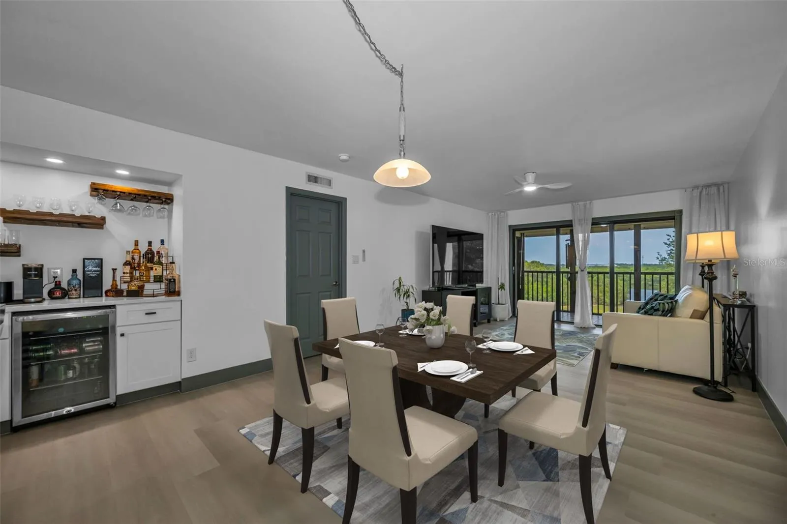 Dining room area with dry bar and wine refrigerator close at hand.  Beyond see living room and private balcony with views beyond.