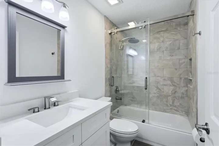 Secondary bathroom with newly tiled shower and glass sliding door as well as a quartz vanity with soft close cabinets and a picture mirror