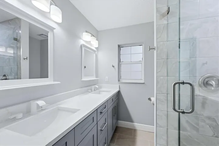 Beautifully upgraded and updated primary bathroom features quartz counters, soft close cabinets and drawers, dual sinks with picture mirrors and white Moen faucets
