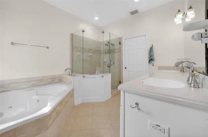 Primary bath with dual sinks, jacuzzi tub, shower and white vanity cabinet