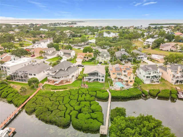 From above, witness the breathtaking harmony of this waterfront home nestled within lush greenery, a true representation of serene coastal life and its enchanting surroundings.