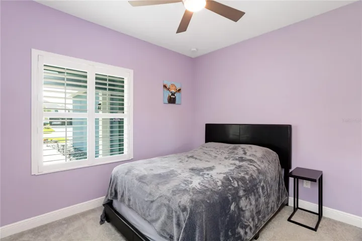 Lavender Guest Bedroom RetreatSoft lavender walls and natural light create a calming guest retreat perfect for visiting family, seasonal residents, or a peaceful secondary bedroom. Plantation shutters, neutral carpeting, and clean modern finishes give this room a bright Florida feel while offering flexibility for guests, hobbies, or a quiet reading space.