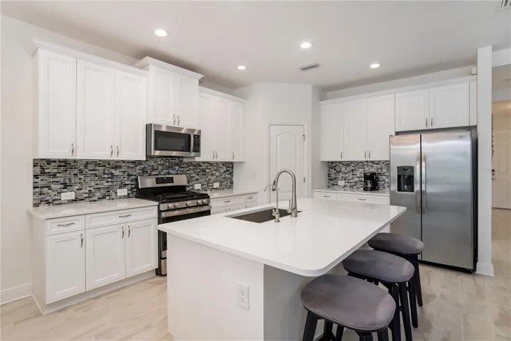 Luxury White Kitchen with Quartz Counters & Large Center IslandChef-inspired kitchen featuring white shaker cabinetry, quartz countertops, stainless steel appliances, designer backsplash, and oversized island seating. A dream kitchen for buyers seeking modern coastal homes with upscale finishes and open entertaining space.