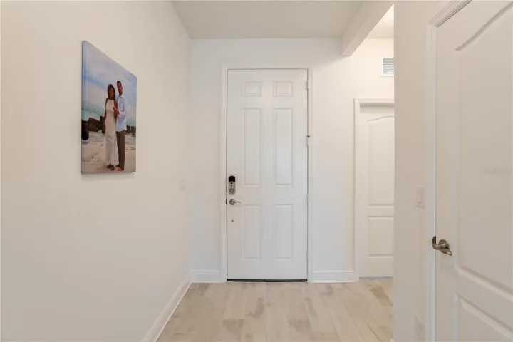 Welcoming Florida Entryway with Light Wood Tile Flooring & Smart Home FeaturesClean and elegant front entry featuring upgraded tile flooring, neutral coastal tones, and a smart entry lock system. This inviting foyer creates a strong first impression for buyers searching for move-in-ready homes with modern finishes in Southwest Florida.