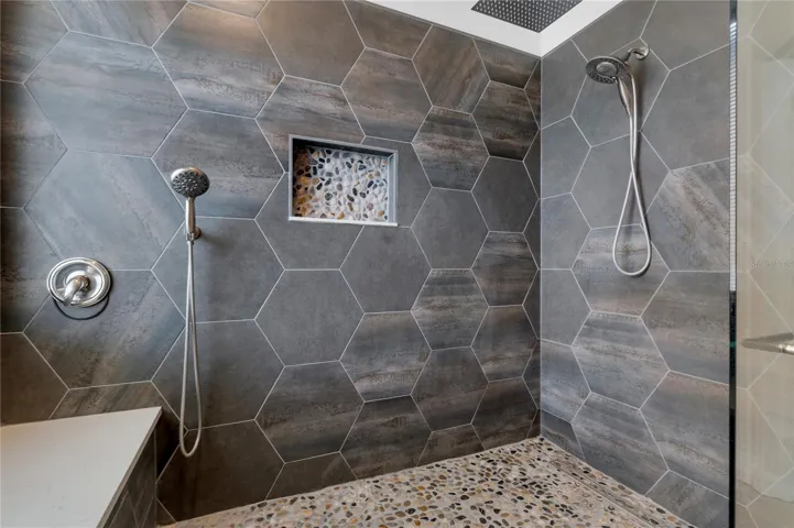 Modern design features rain shower head plus his and hers shower heads and bench.