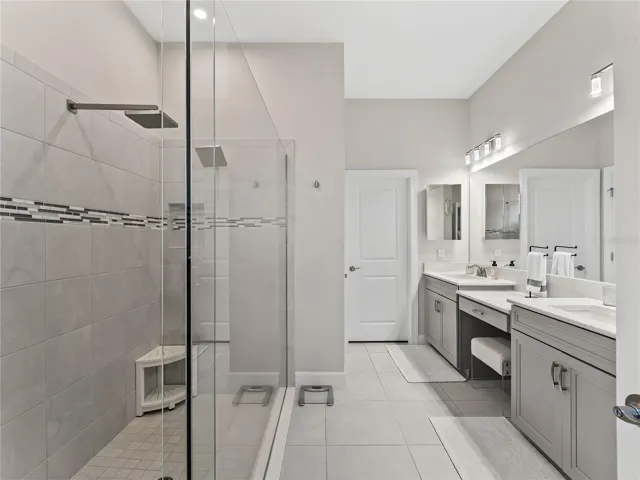 The primary bathroom offers a spa-like retreat, featuring a large walk-in shower with dual rain showerheads, double vanity sinks, and a makeup vanity.