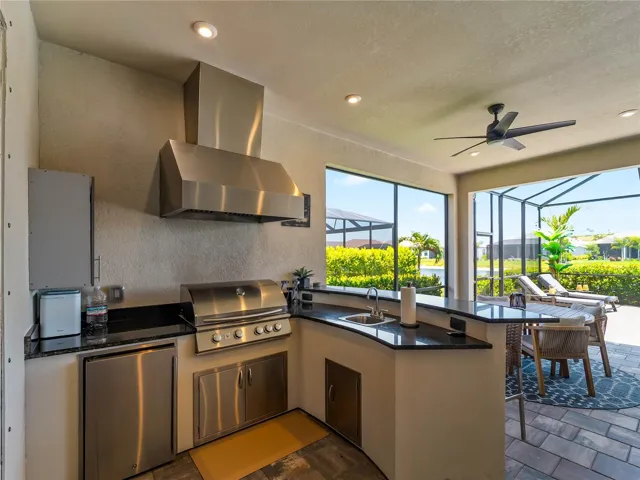 The outdoor kitchen features a grill, refrigerator, and bar-height seating.