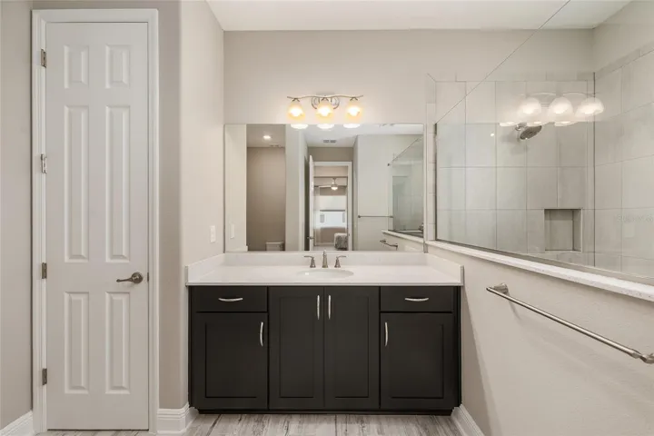 Second primary bathroom ensuite featuring a spacious vanity with abundant storage, large mirror, linen closet, neutral finishes, and a private bath layout for added comfort and convenience.