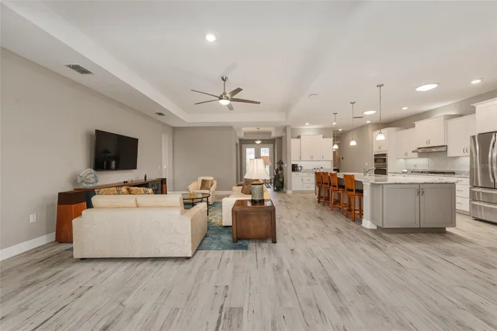 Open-concept great room, dining area, and kitchen featuring ceramic plank flooring, neutral finishes, recessed lighting, a tray ceiling in the great room, and two solar tubes in the kitchen for added natural light.