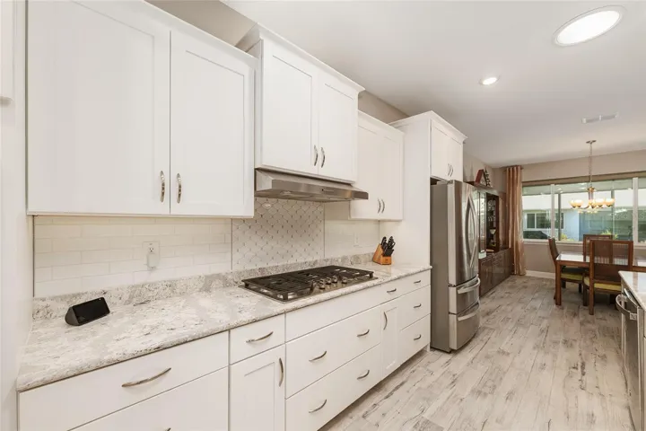 Kitchen view featuring abundant pot drawers, stainless steel appliances, 5-burner gas cooktop, neutral backsplash, Cambria Quartz island, and open flow into the dining room.